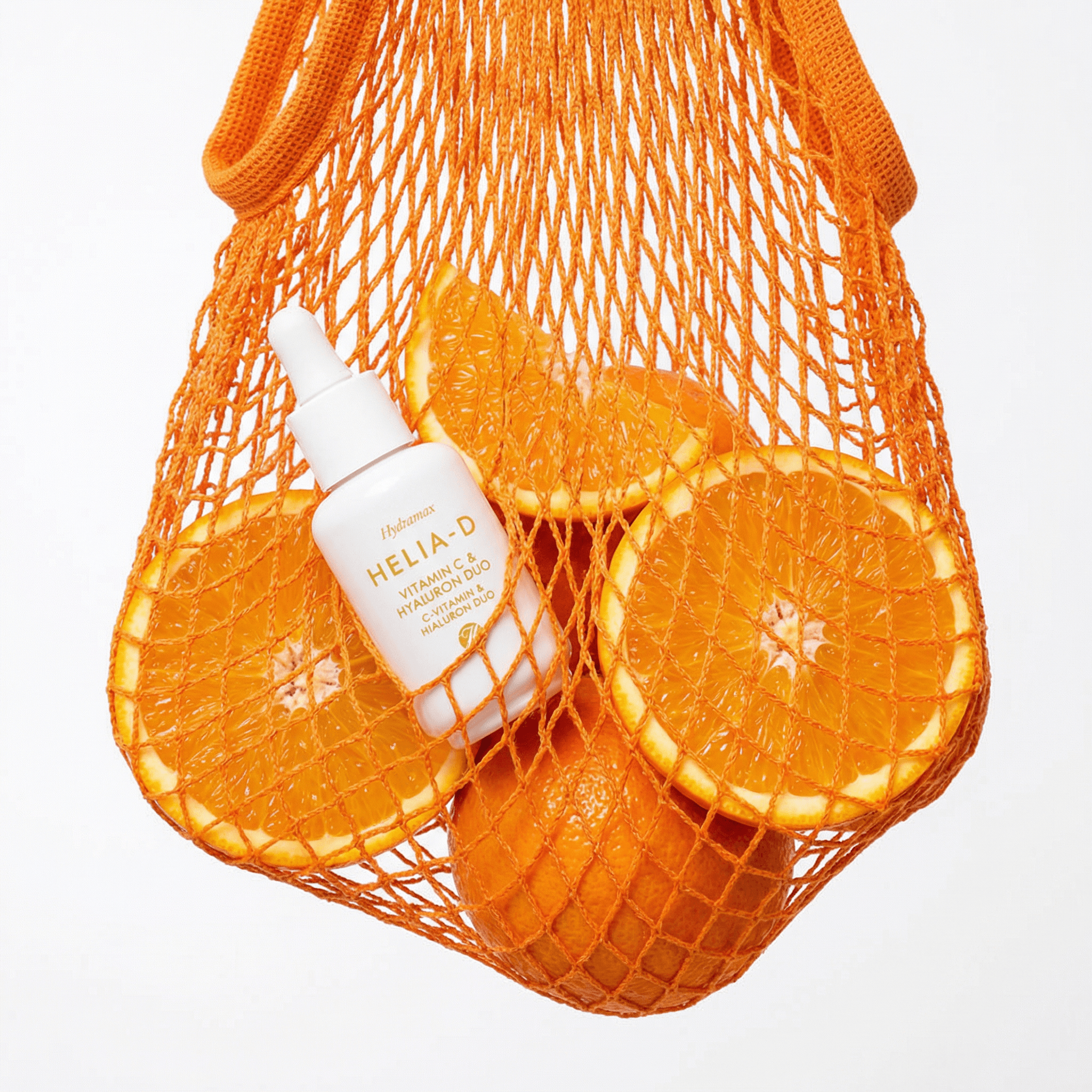 The image is a fresh, graphic still life that blends skincare with everyday grocery imagery.
A vitamin C serum bottle is tucked inside a bright orange mesh produce bag alongside sliced oranges. The bag hangs suspended against a clean white background, giving the composition a light, weightless feel. The mesh partially obscures the objects, adding texture and visual rhythm while still keeping the product clearly readable.
The oranges act as a literal ingredient cue, reinforcing the vitamin C concept through color and form. Their glossy, juicy surfaces contrast with the matte bottle and the soft translucency of the netting.
Lighting is bright and even, emphasizing saturation and clarity without harsh shadows. The palette is tightly controlled—orange on white—making the image feel bold, modern, and instantly legible.
Overall, the image feels clever, playful, and ingredient-forward, using a familiar object (a produce bag) to communicate freshness, efficacy, and simplicity in a contemporary skincare context.