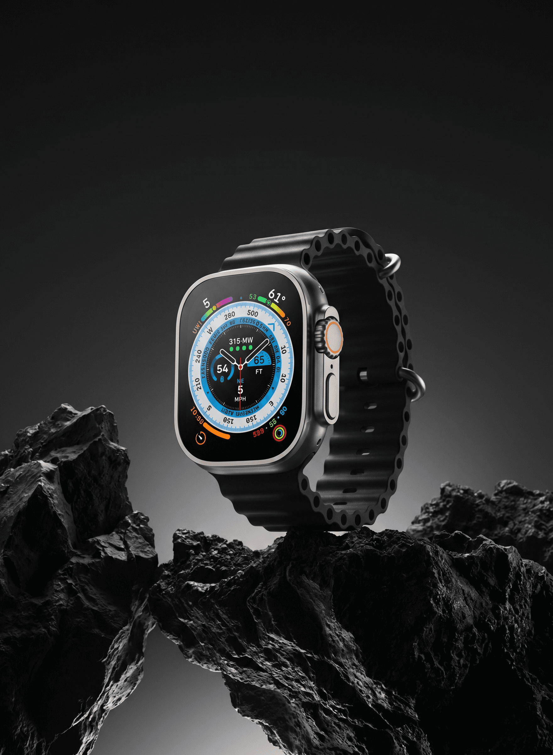 Rugged adventure editorial, Apple Watch Ultra standing upright on jagged dark volcanic rocks against a deep charcoal-to-black gradient studio background, the titanium case gleaming against the raw textured stone, the vivid multicolored Wayfinder compass face blazing with blues, greens and oranges in sharp detail, dramatic gradient underlighting sculpting the rocks, powerful outdoor premium positioning of an extreme adventure instrument