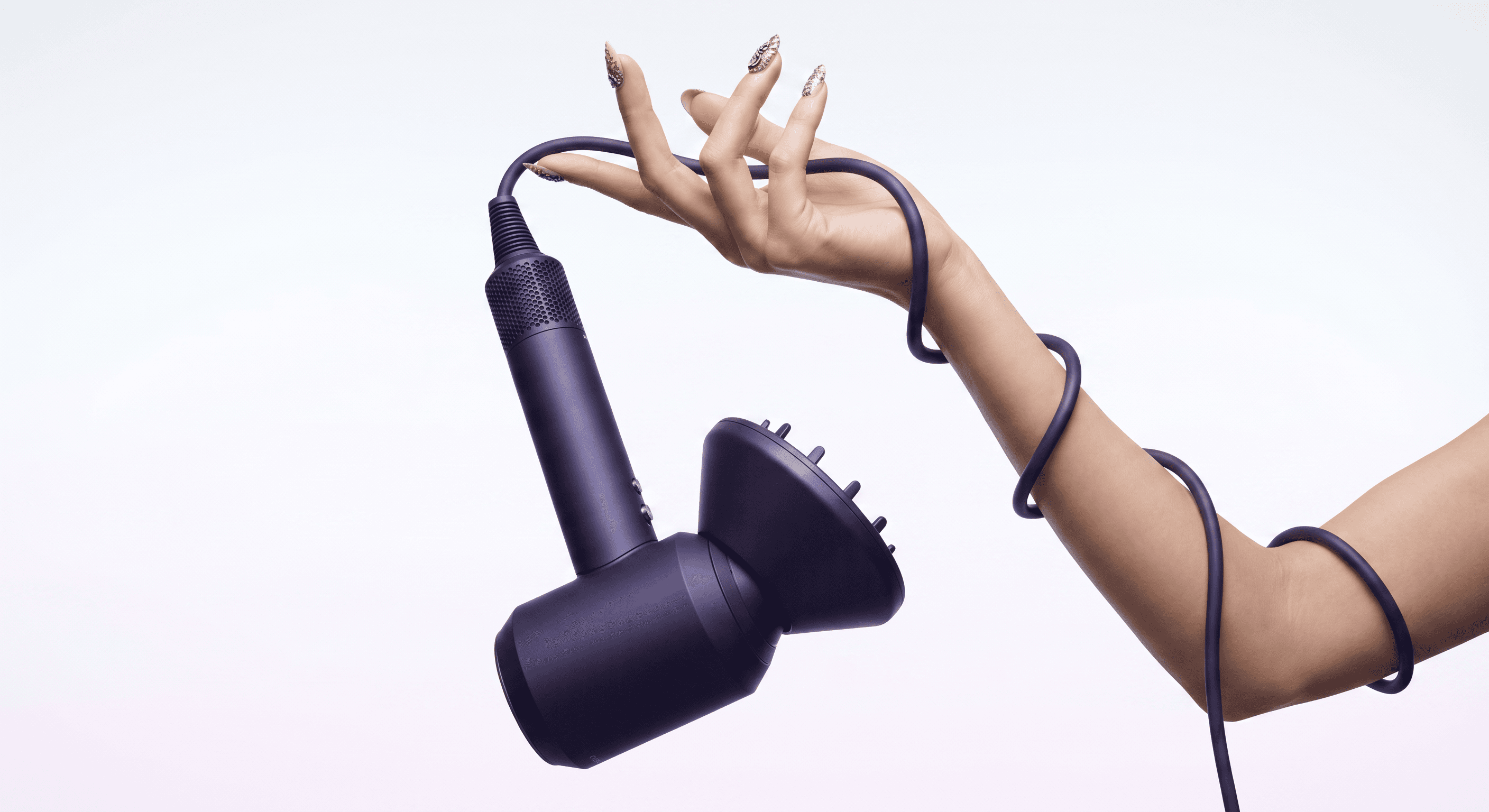 High-fashion editorial, matte dark purple Dyson Supersonic hair dryer with diffuser attachment dangling from a woman's hand in an inverted downward angle, intricate nail art adorning elegant fingers, the power cord wrapping sensuously up the forearm creating a dynamic compositional flow, clean white-to-light gradient background, editorial luxury beauty meets industrial design, the unconventional angle making the product utterly covetable