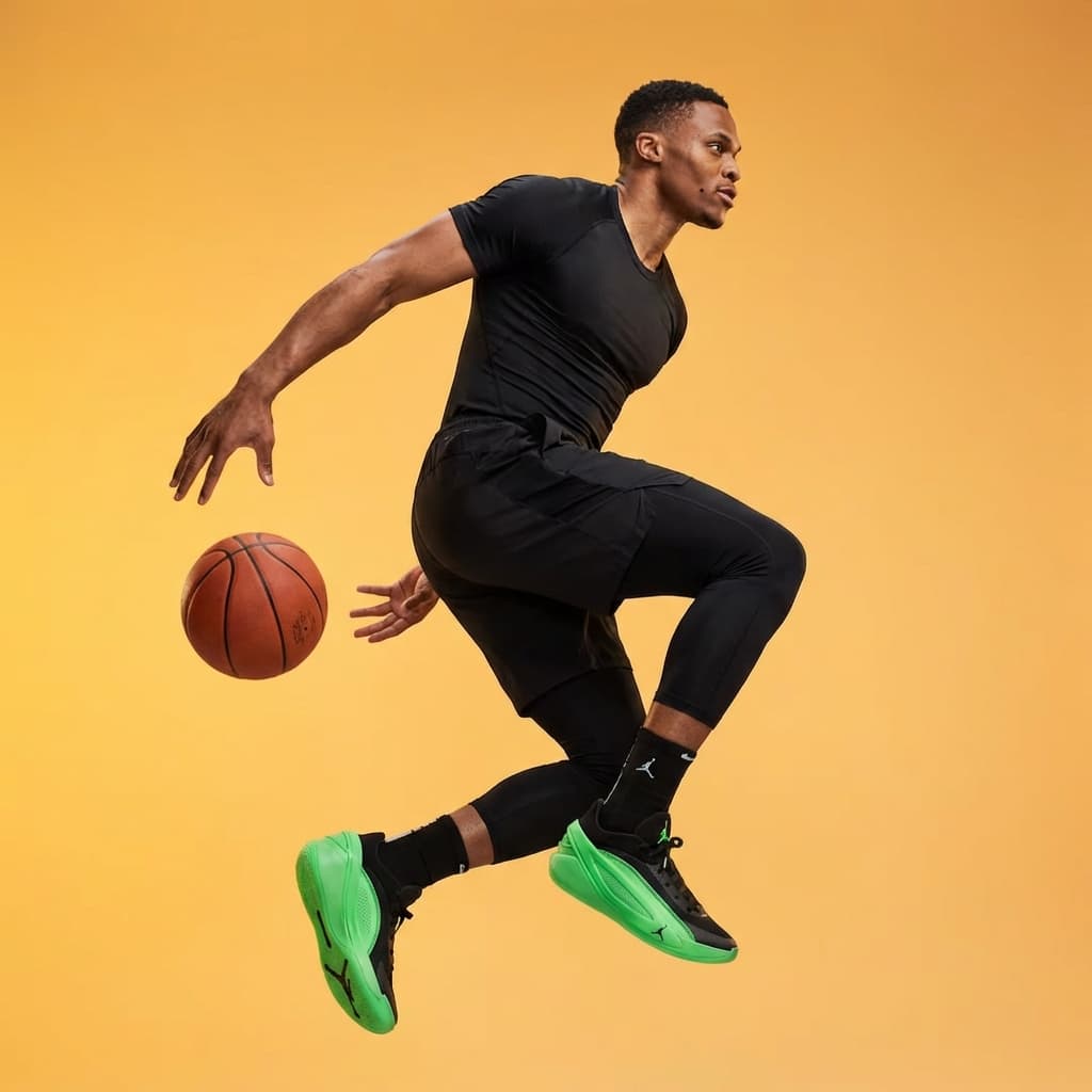 The photo captures an athletic, high-energy moment frozen in mid-action.
A male athlete is suspended in the air, knees bent and body twisted, as if changing direction or preparing to pass. One hand trails behind him while a basketball floats nearby, reinforcing the sense of motion and timing. The pose feels dynamic and controlled rather than chaotic.
He wears fitted performance apparel—shorts layered over leggings and lightweight trainers—emphasizing speed, flexibility, and strength. The footwear, with its bright green soles, adds a sharp visual accent against the otherwise dark outfit.
The background is a smooth, seamless gradient shifting from warm yellow to orange, creating a bold, studio-controlled environment with no external context. The lighting is even and bright, sculpting the body without harsh shadows and keeping all details crisp despite the implied movement.
Overall, the image feels energetic, modern, and promotional, blending sports performance with fashion-driven studio aesthetics.